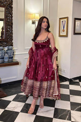 Woman in a maroon traditional outfit standing in a room with checkered floor and decorative elements.