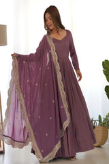 Woman wearing a long purple dress with gold embroidery in a bright room.