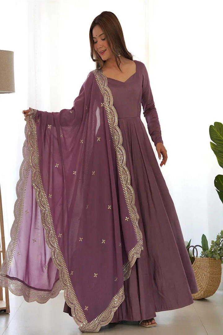 Woman wearing a long purple dress with gold embroidery in a bright room.