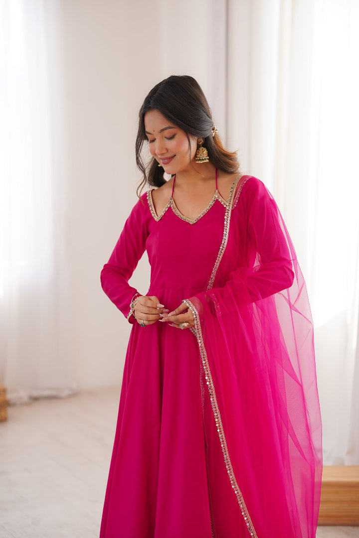 Woman wearing a bright pink traditional outfit with gold details indoors.