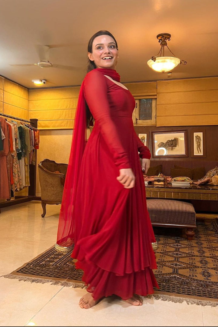 Woman in a red dress standing in a room with a rack of clothes and furniture.