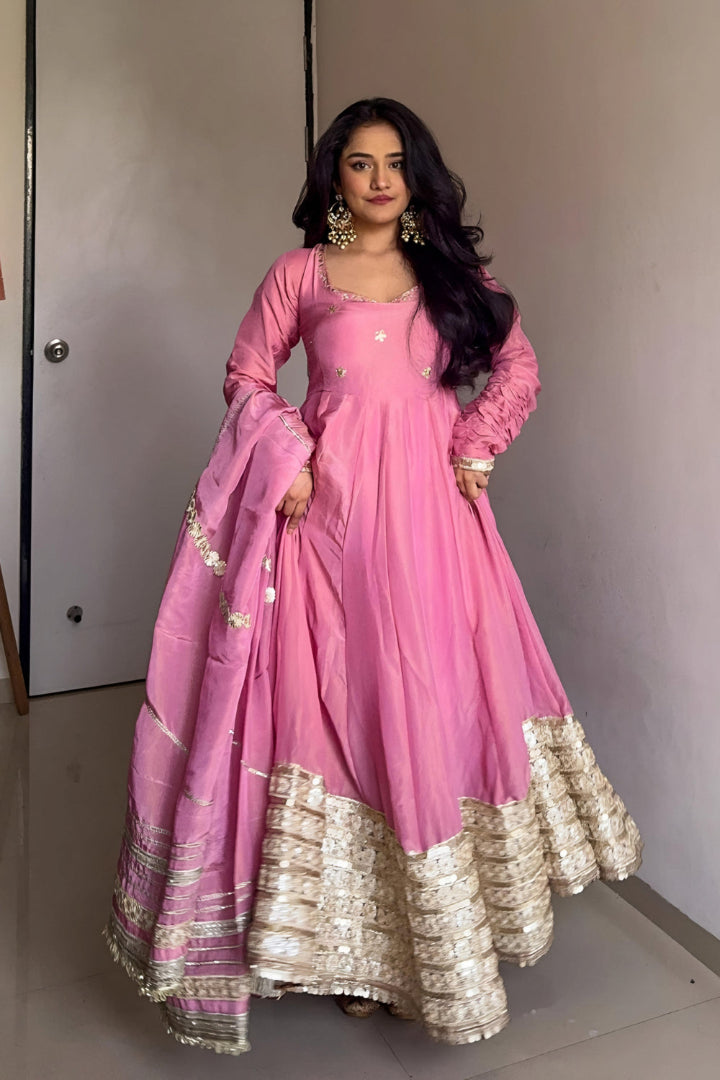 Woman in a pink traditional outfit with gold details against a neutral background
