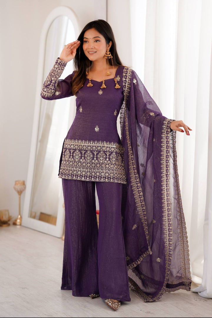 Woman in a purple traditional outfit with gold details standing in a bright room.