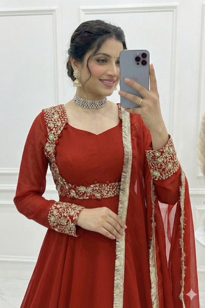 Woman in a red traditional outfit with gold details taking a mirror selfie.