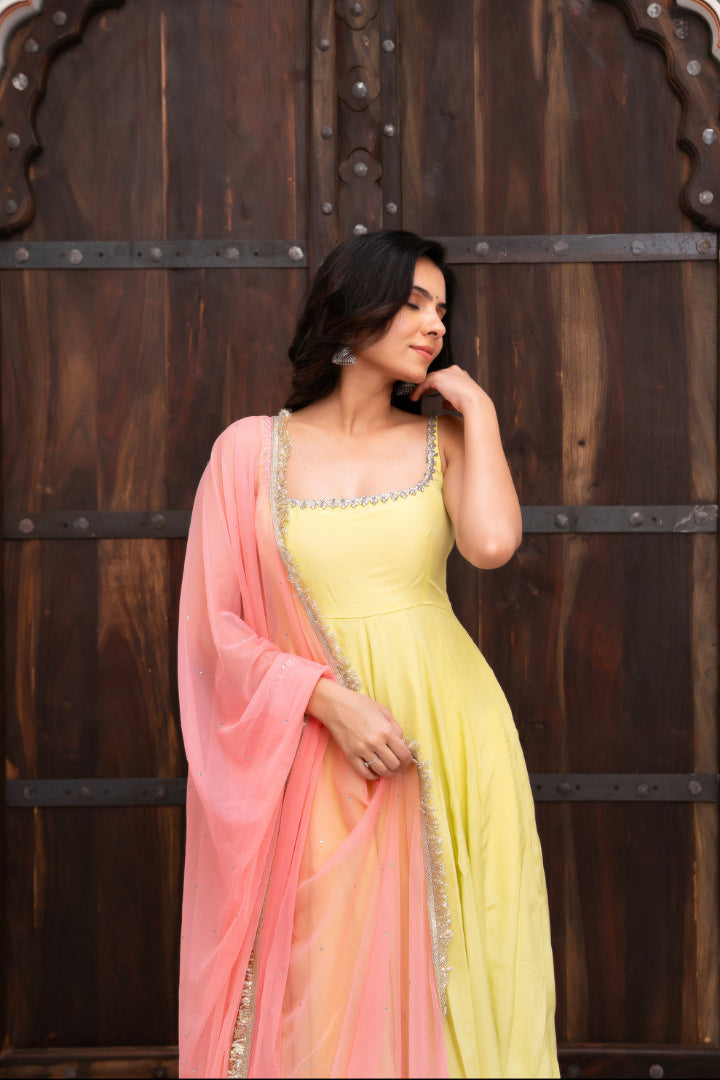 Woman in a yellow and pink saree standing in front of a wooden door with intricate carvings.