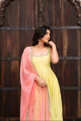 Woman in a yellow and pink saree standing in front of a wooden door with intricate carvings.