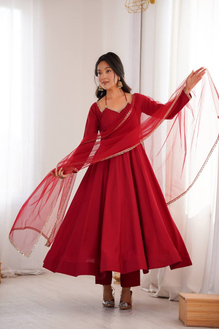 Woman in a red dress with a sheer dupatta against a white curtain background