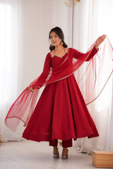 Woman in a red dress with a sheer dupatta against a white curtain background