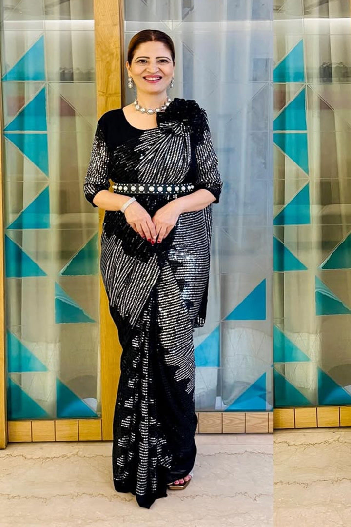 Woman in a black and white patterned saree standing in front of a geometrically patterned wall.