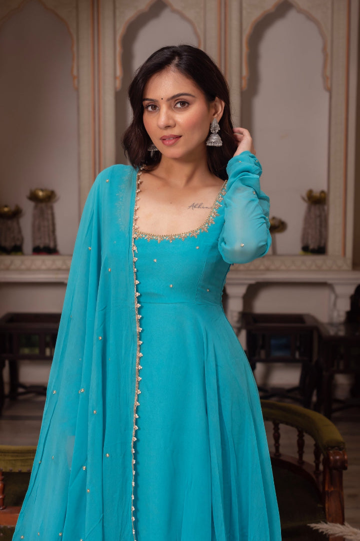 Woman in a turquoise traditional outfit with a matching dupatta indoors.