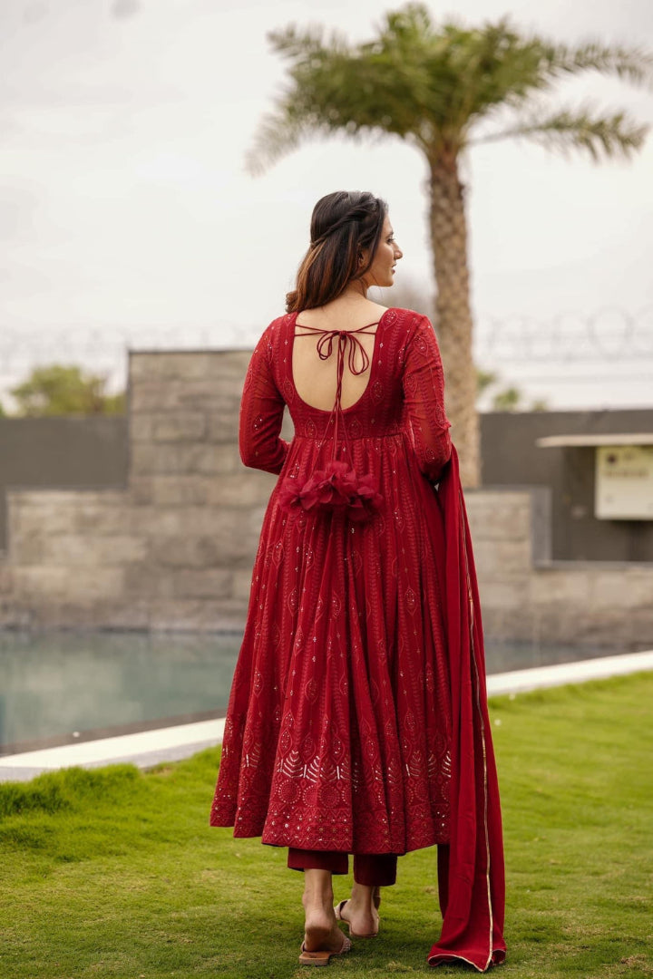 Woman in a red dress standing on grass with a pool and palm tree in the background