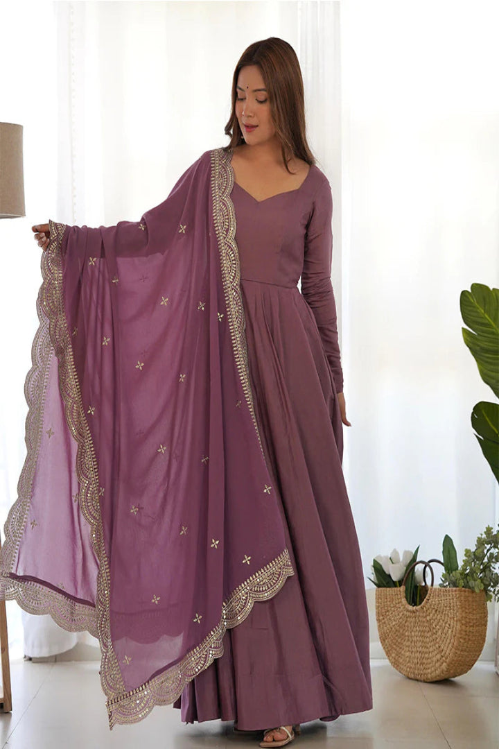 Woman wearing a long purple dress with a matching dupatta in a bright room.