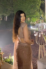 Woman in a sparkling outfit standing outdoors with decorative lights and greenery.