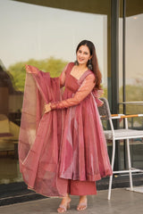 Woman in a pink traditional outfit holding a dupatta, standing in front of a glass door.