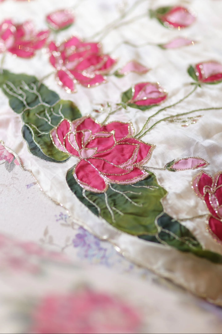 Close-up of floral embroidery on saree with pink flowers and green leaves.