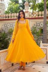 Woman in a yellow traditional outfit standing in front of decorative architecture.