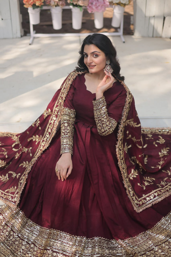 Woman in a maroon traditional outfit with gold embroidery indoors.