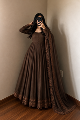 Person wearing a brown dress with lace details in a room.