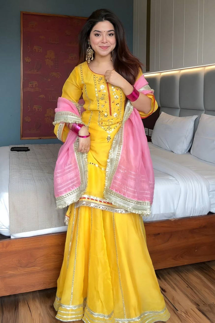 Woman in a yellow and pink traditional outfit standing in a bedroom.