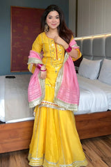 Woman in a yellow and pink traditional outfit standing in a bedroom.