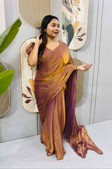 Woman in a maroon and gold saree standing in front of decorative wall art.