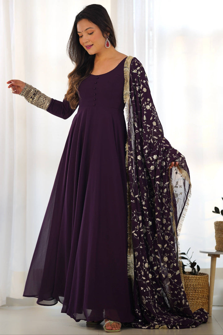 Woman wearing a long purple dress with a floral dupatta in a bright room.
