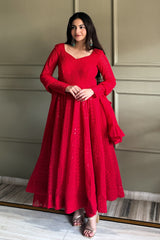 Woman wearing a red dress standing against a neutral wall.