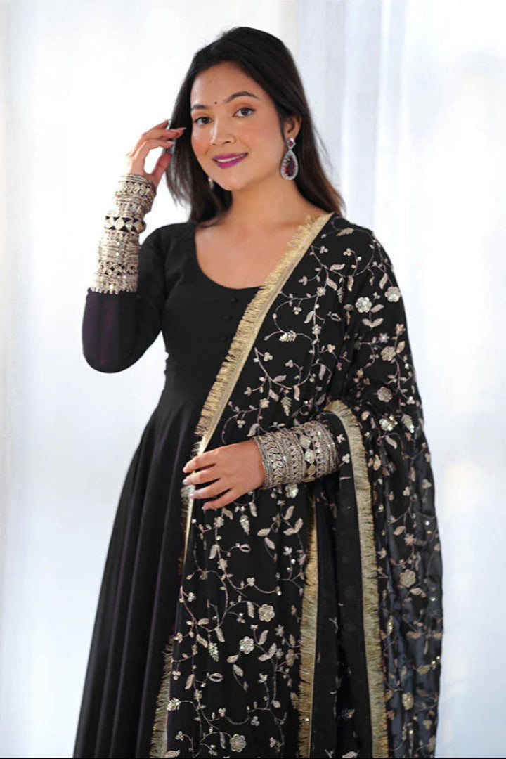 Woman wearing a black traditional outfit with a floral dupatta against a white background