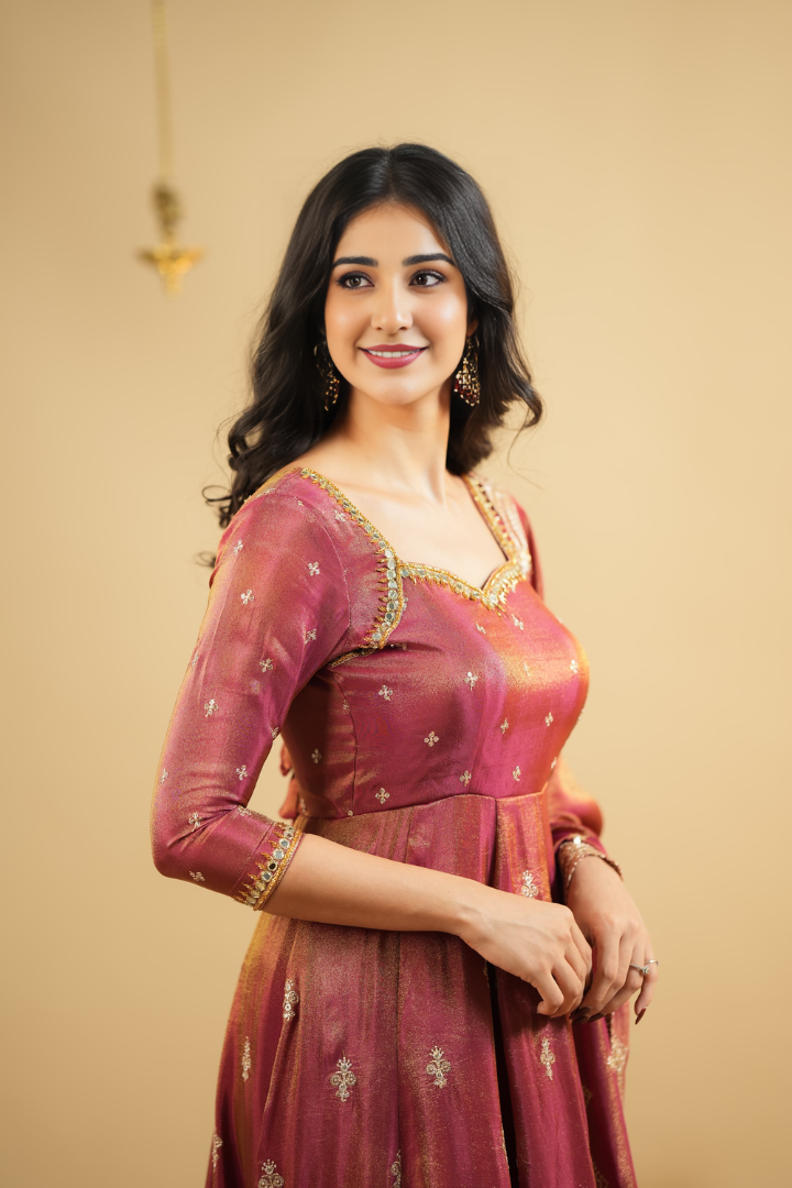 Woman wearing a traditional maroon saree with gold details against a beige background