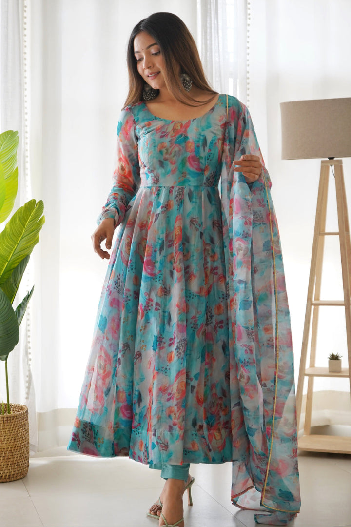 Woman wearing a colorful floral dress in a bright room with plants and a lamp.