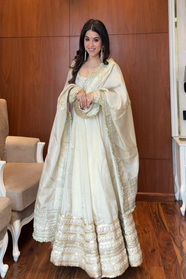 Woman in a white traditional outfit with gold details in an indoor setting.