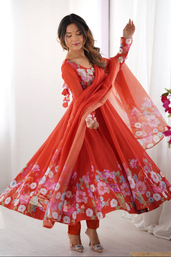 Woman in a red floral traditional outfit standing in a bright room with white curtains.