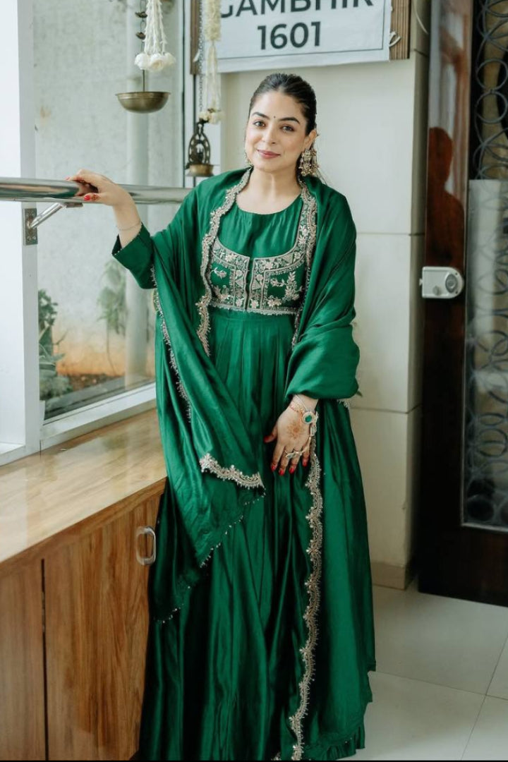 Woman in a green traditional outfit standing indoors with decorative elements.