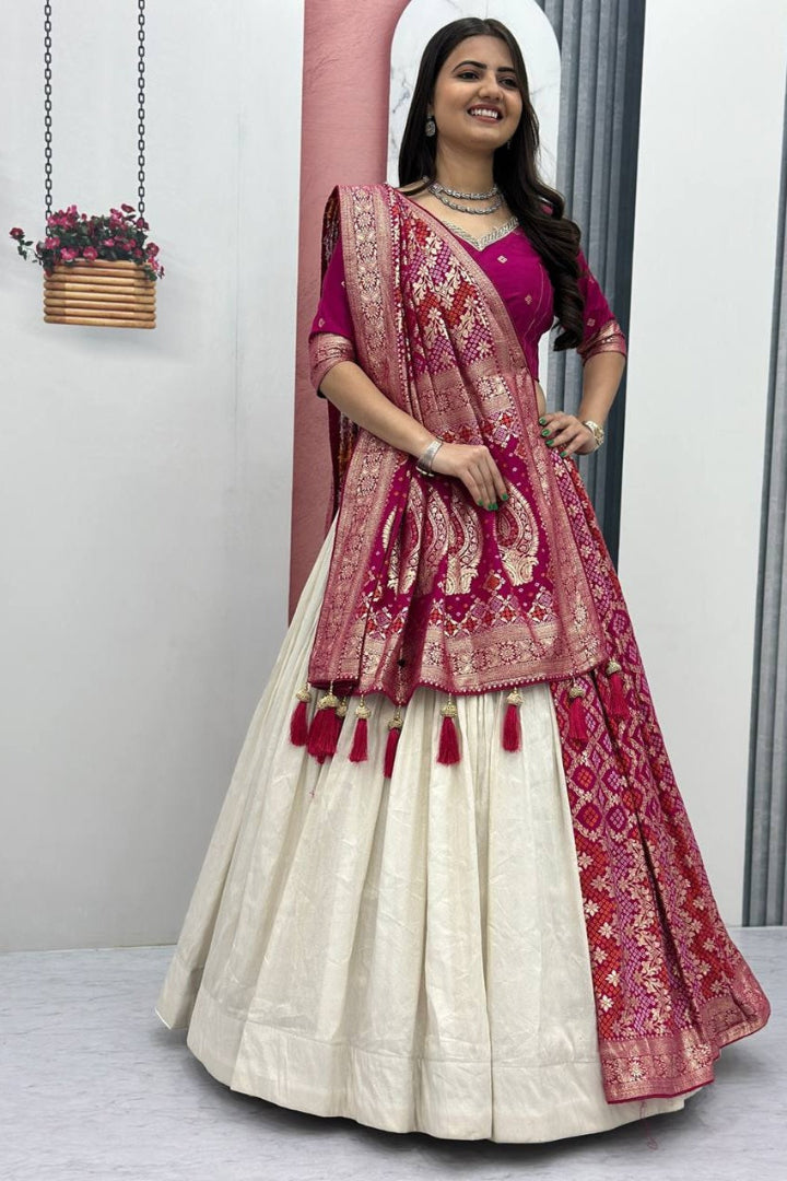 Woman wearing a traditional outfit with a pink and red dupatta in a minimal indoor setting.