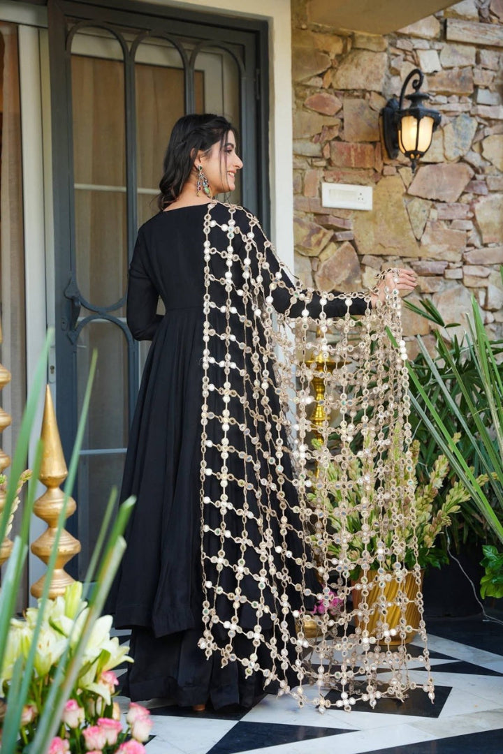 Woman holding a decorative curtain in front of a stone wall and door.