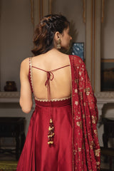 Woman in a red saree with gold details, standing in an indoor setting.
