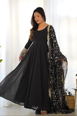 Woman wearing a black dress with a floral dupatta in a bright room.