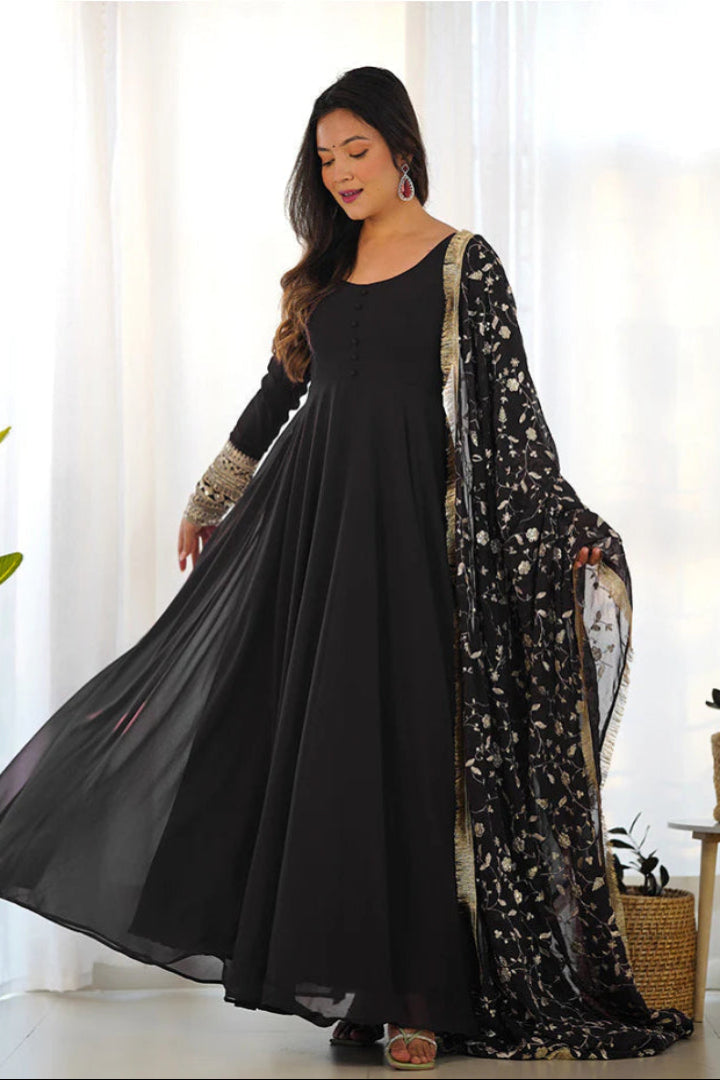 Woman wearing a black dress with a floral dupatta in a bright room.