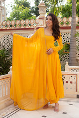 Woman in a yellow traditional outfit standing on a decorative balcony with greenery in the background