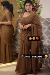 Woman wearing a brown saree with gold embroidery, standing in front of a decorated Christmas tree.