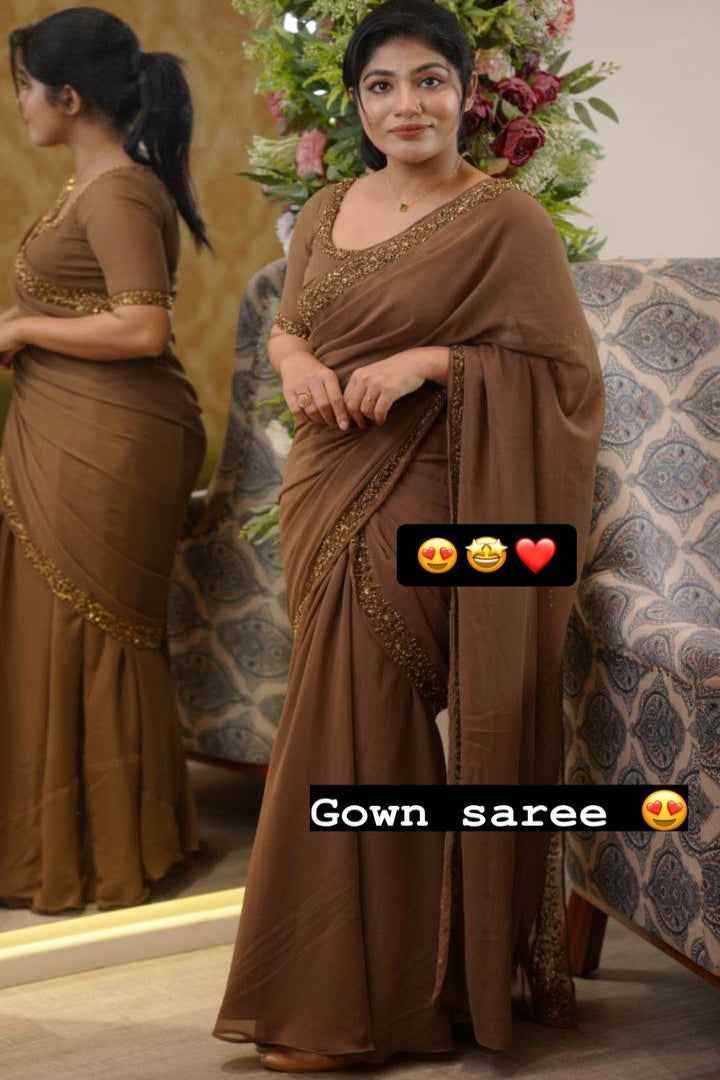 Woman wearing a brown saree with gold embroidery, standing in front of a decorated Christmas tree.