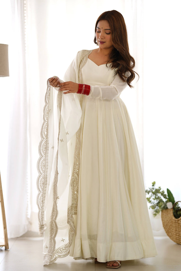 Woman in a white traditional outfit with a long scarf indoors.
