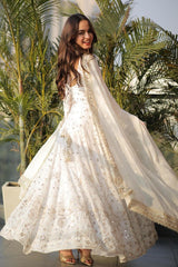 Woman in a white embroidered dress standing outdoors with greenery in the background