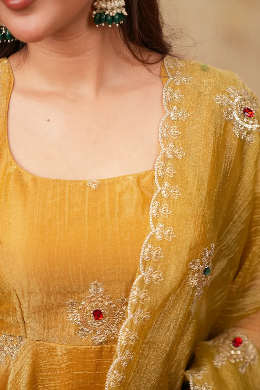 Close-up of a mustard yellow traditional outfit with intricate silver embroidery and red and green stone accents, worn by a model.