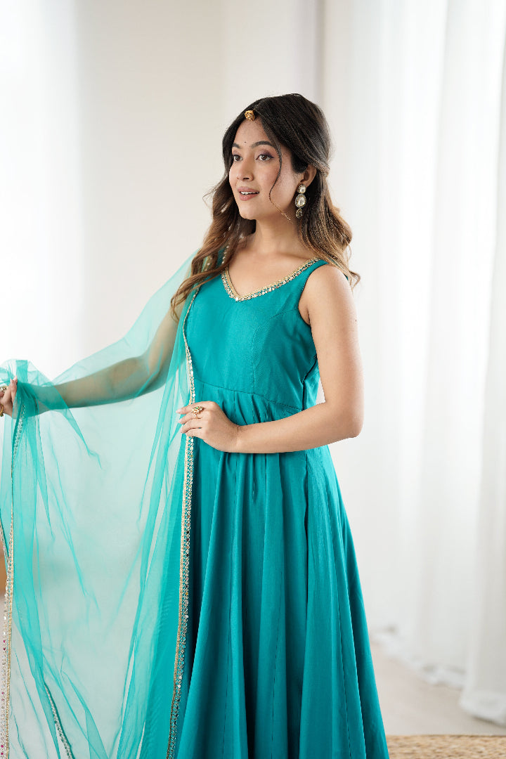 Woman in a teal dress holding a matching dupatta against a white background