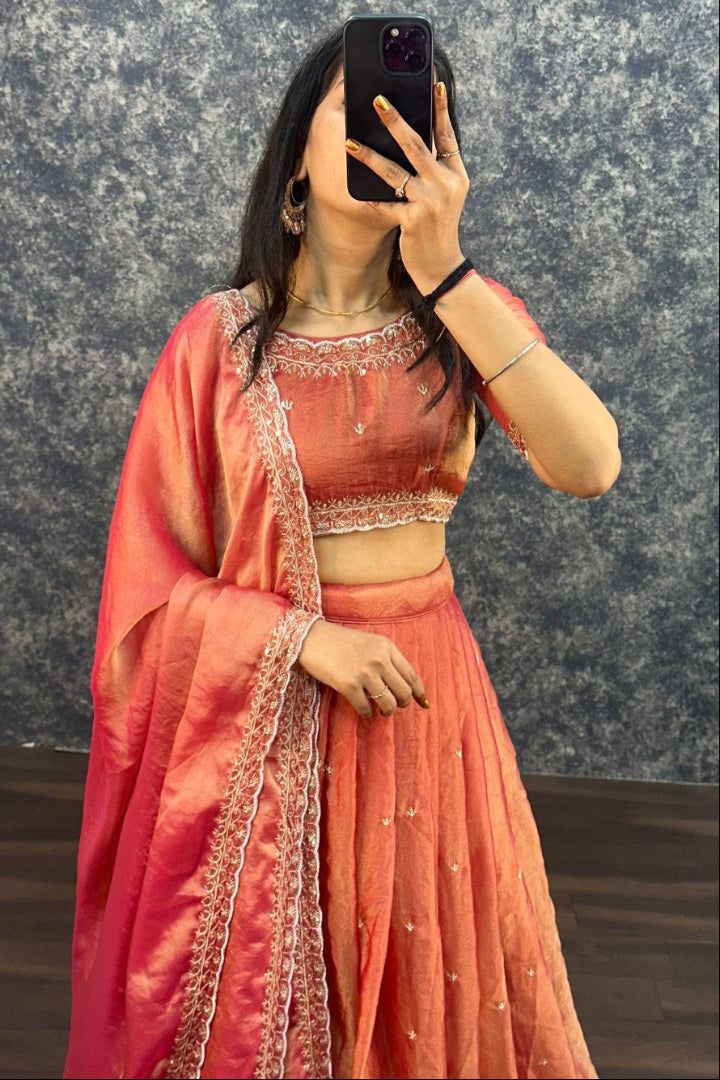 Person wearing a traditional pink saree with intricate designs against a textured wall.
