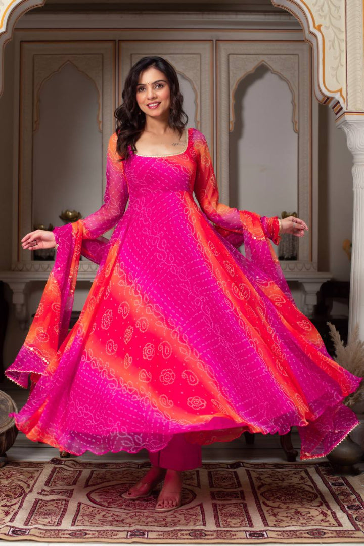 Woman in a vibrant pink and orange traditional outfit standing in an ornate room.