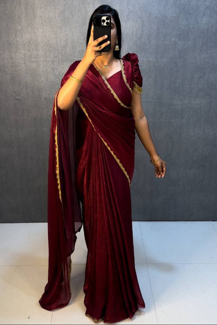 Person wearing a maroon saree with gold border against a plain background