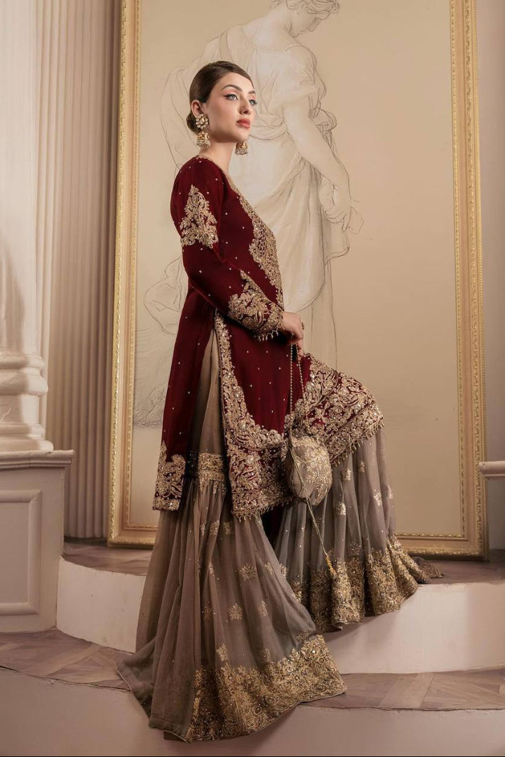 Woman in a burgundy and gold embroidered traditional outfit standing in an elegant interior setting.