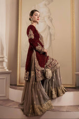 Woman in a burgundy and gold embroidered traditional outfit standing in an elegant interior setting.